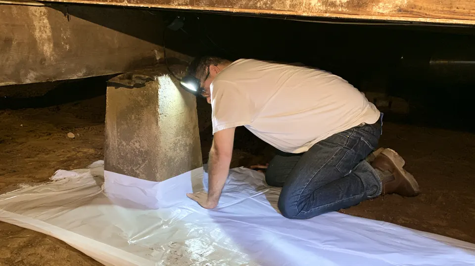 A sealed white liner covering the dirt floor of a crawl space under a pier and beam home during crawl space encapsulation in McKinney.
